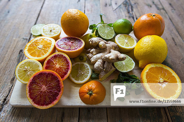 Geschnittene und ganze Zitronen  Orangen und Limetten  Ingwerwurzel und Minzblätter auf Holzbrettchen