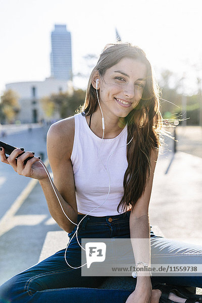 Spain  Barcelona  portrait of smiling young woman relaxing at sunset listening music with earphones