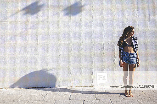 Junge hübsche Frau in Strandkleidung vor weißer Wand stehend