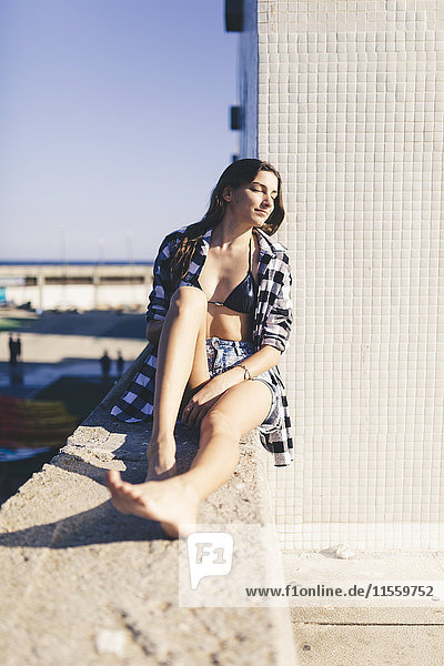 Young pretty woman wearing beach wear sitting on wall