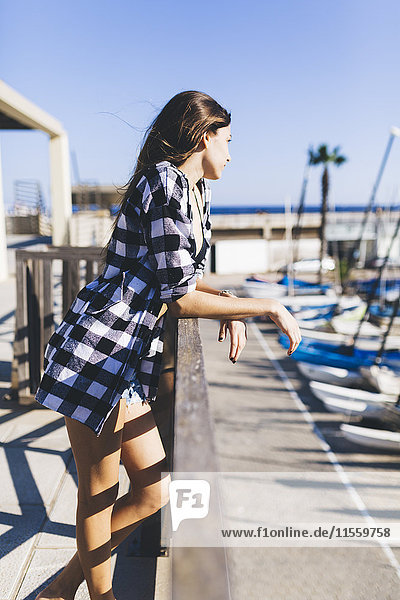 Junge hübsche Frau in Strandkleidung an der Balustrade am Hafen stehend