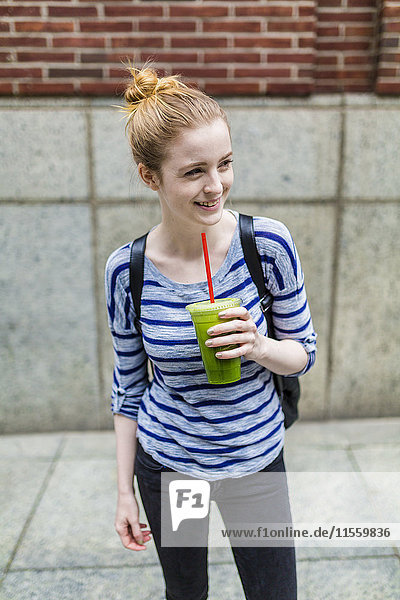 Lächelnde junge Frau trinkt einen Smoothie im Freien