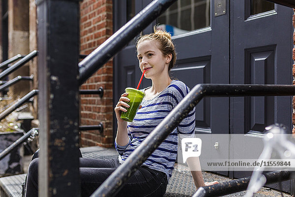 USA  New York City  Frau  die in Manhattan auf der Treppe sitzt und einen Smoothie trinkt.