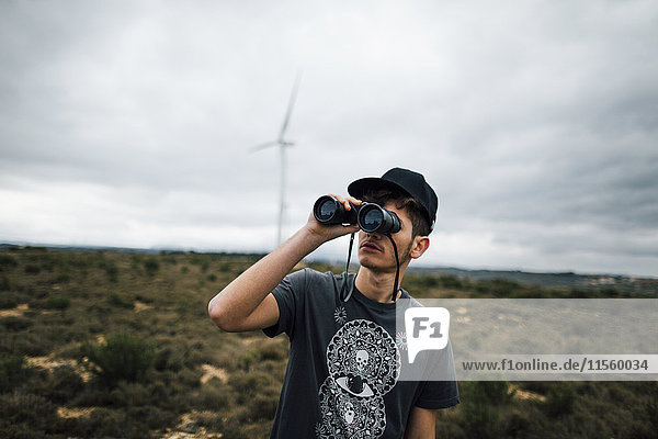 Spanien  Lleida  junger Mann schaut durchs Fernglas in ländlicher Landschaft