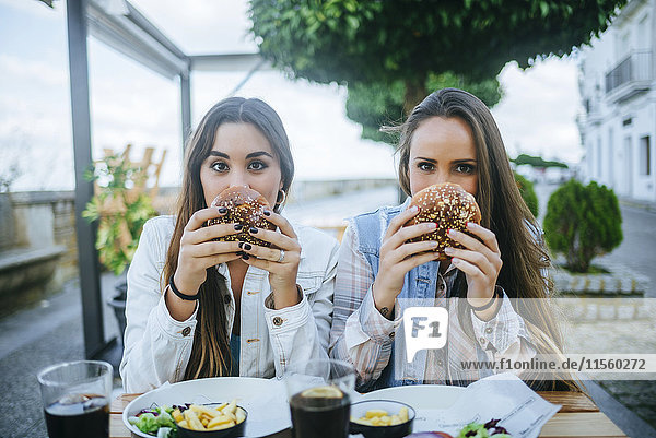 Portrait of two women holding hamburgers in a street restaurant