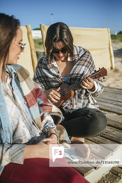 Woman playing ukulele on the beach while her friend watching her