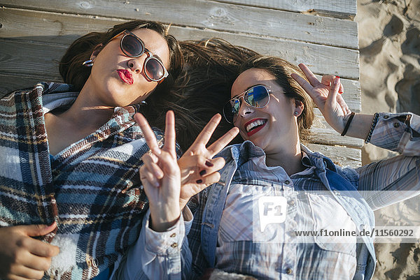 Two young women lying on wooden boardwalk showing victory signs