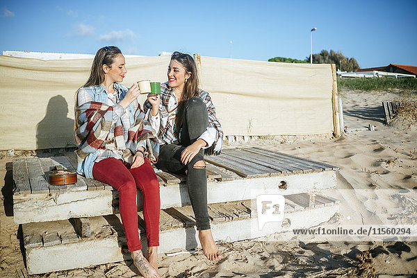 Two young women drinking coffee on the beach