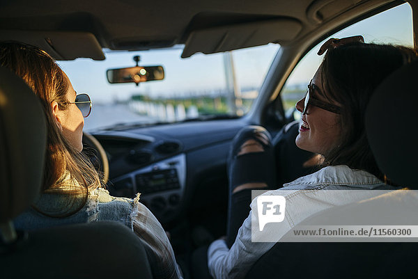 Zwei junge Frauen mit Sonnenbrille entspannen sich in der Abenddämmerung im Auto.