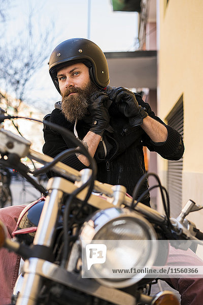 Portrait of bearded biker fastening helmet while sitting on his motorcycle