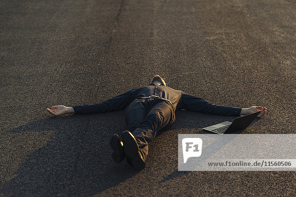 Businessman lying on a road next to laptop
