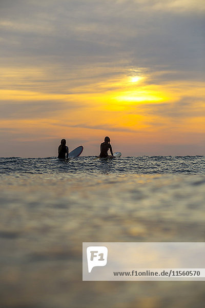 Indonesien  Bali  zwei Surferinnen im Meer bei Sonnenuntergang