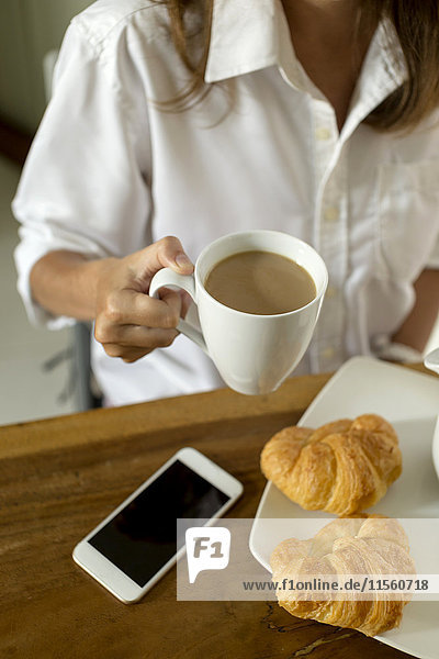Frau am Frühstückstisch mit Kaffee  Croissants und Handy