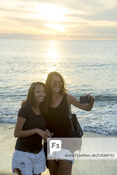 Indonesien  Bali  zwei Frauen mit einem Selfie am Strand bei Sonnenuntergang