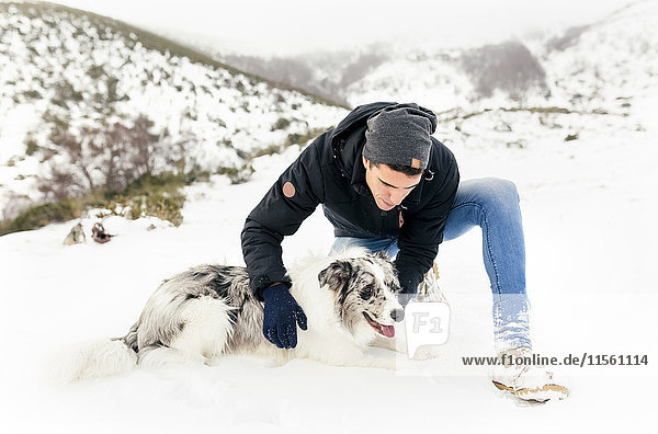 Junger Mann streichelt seinen Hund im Schnee