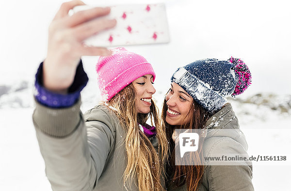 Zwei Freunde,  die sich mit dem Smartphone im Schnee austoben
