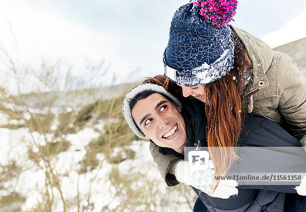 Junger Mann trägt sein Mädchen im Winter gebratenes Huckepack