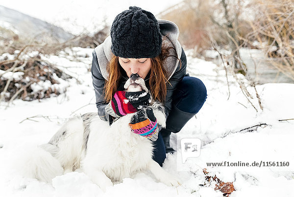 Young woman kissing her dog in the snow