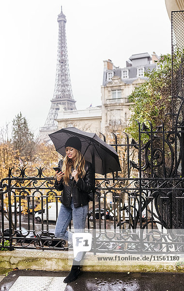 Frankreich  Paris  junge Frau mit ihrem Smartphone mit dem Eiffelturm im Hintergrund