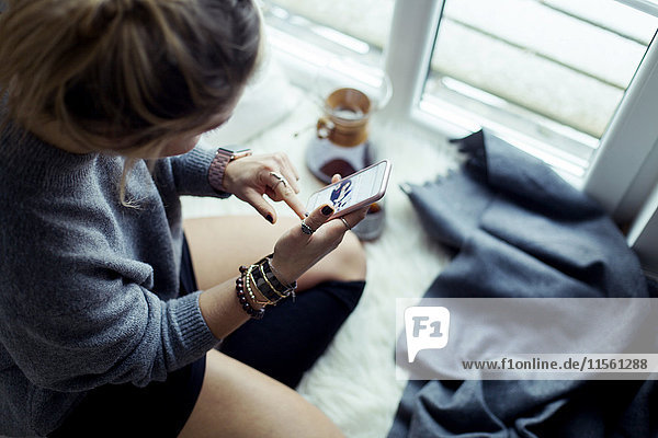 Junge Frau entspannt auf Schaffell zu Hause mit dem Handy