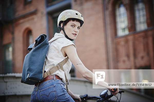 Portrait einer jungen Frau mit Fahrradhelm und Rucksack auf Elektrofahrrad