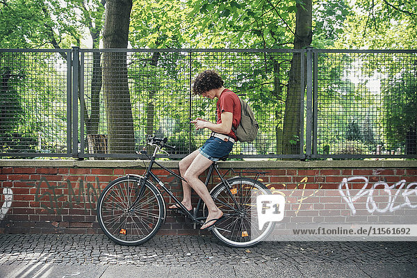 Junger Mann mit Handy auf dem Fahrrad sitzend