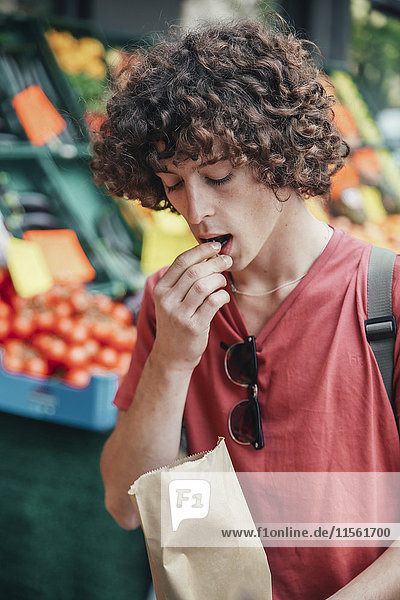 Young man eating cherries in front of street fruit stand