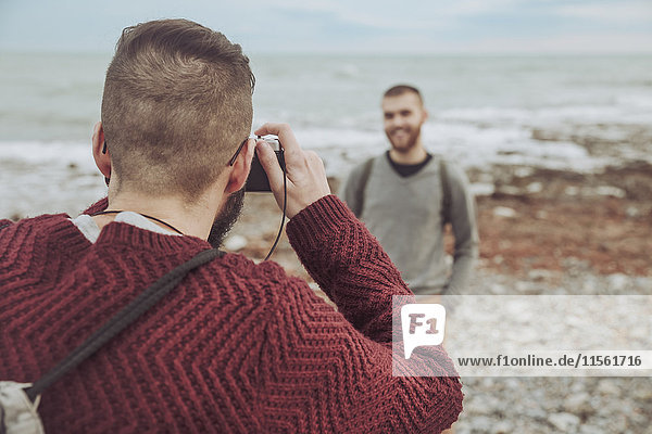 Mann  der seinen Freund vor dem Meer fotografiert.