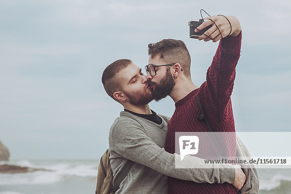 Schwules Paar  das sich beim Küssen vor dem Meer selbst küsst.