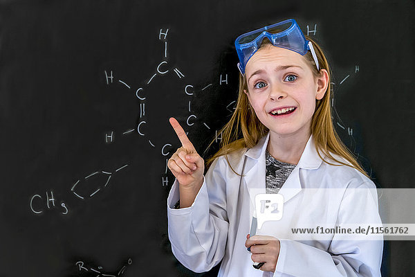Porträt des Mädchens mit Arbeitsmantel und Schutzbrille vor der Tafel mit chemischen Formeln