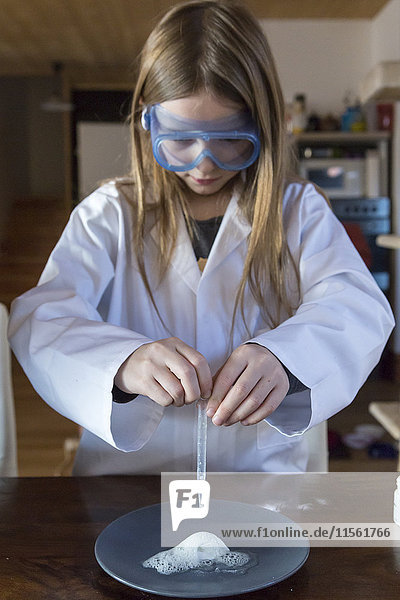 Mädchen in Arbeitsmantel und Schutzbrille mit Chemie-Set zu Hause