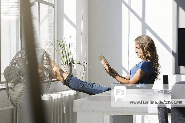 Casual businesswoman in office using digtal tabet with feet on window sill