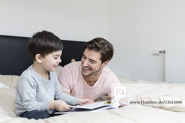 Glücklicher Vater und Sohn beim Lesen eines Buches im Bett