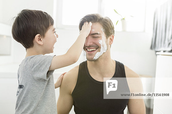 Verspielter Sohn trägt Rasierschaum auf Vaters Gesicht auf.