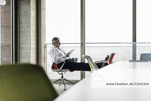 Senior Manager im Büro sitzend auf Stühlen mit erhobenen Füßen mit digitalem Tablett