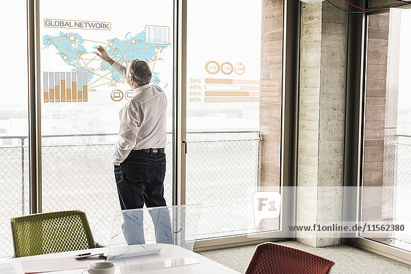 Businessman touching windowpane with world map and global network in office