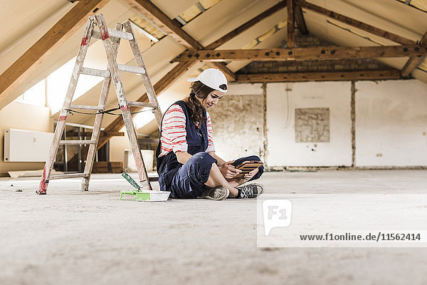 Young woman sitting on construction site  looking on her digital tablet