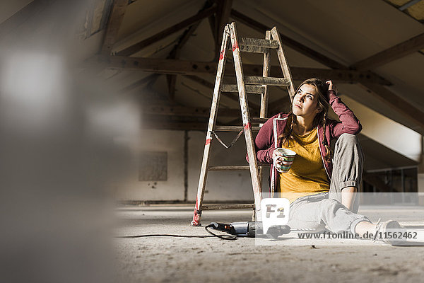 Unabhängige junge Frau renoviert ihr neues Zuhause  sitzt auf dem Boden mit einer Tasse Kaffee.