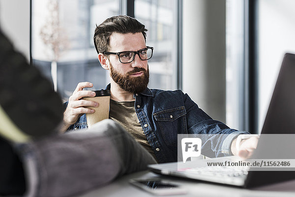 Young casual businessman sitting in office with feet up and a cup of coffee