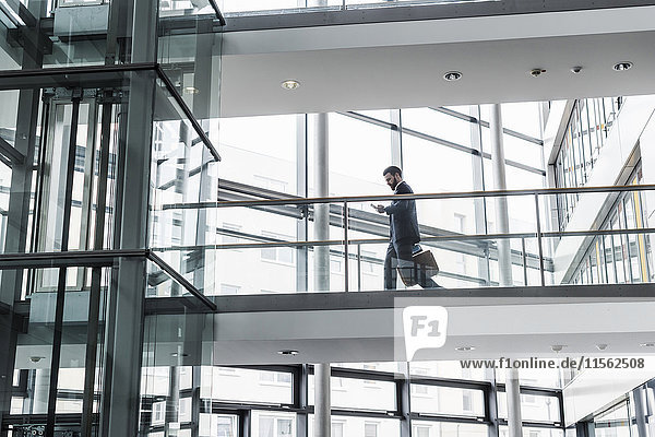 Geschäftsmann  der im Bürogebäude spazieren geht  während er ein Smartphone benutzt.