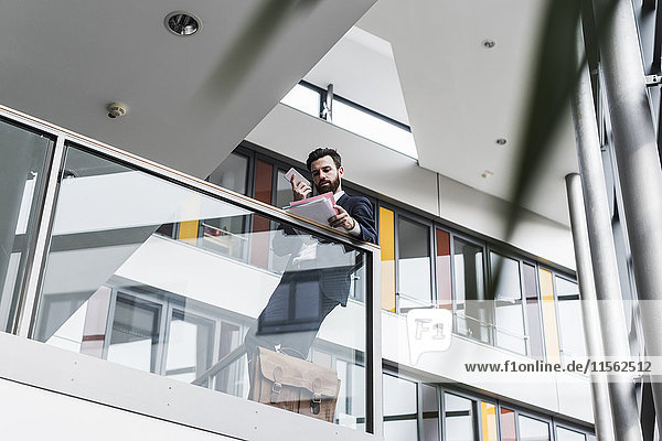 Geschäftsmann auf der Landung eines Bürogebäudes stehend  telefonierend  beim Lesen von Dokumenten