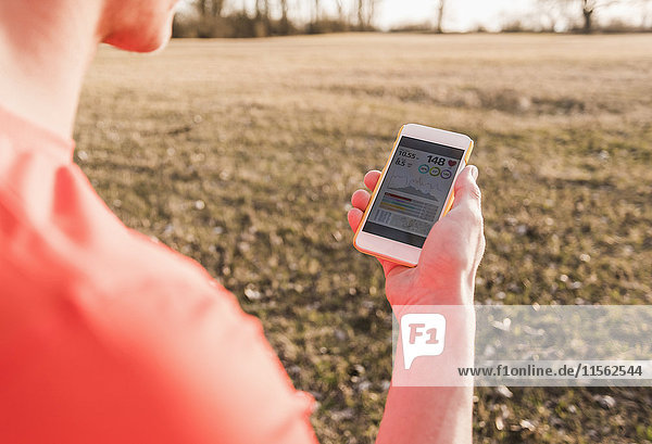 Sportler in ländlicher Landschaft prüft Daten auf dem Handy