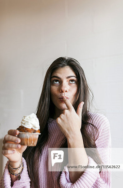 Junge Frau beim Essen einer Tasse Kuchen mit Schlagsahne  Finger lecken