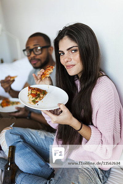 Junges Paar sitzt zu Hause und isst Pizza.
