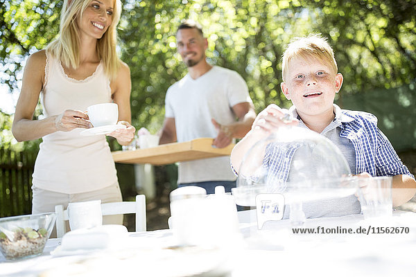 Lächelnder Junge mit seinen Eltern beim Gartentischdecken