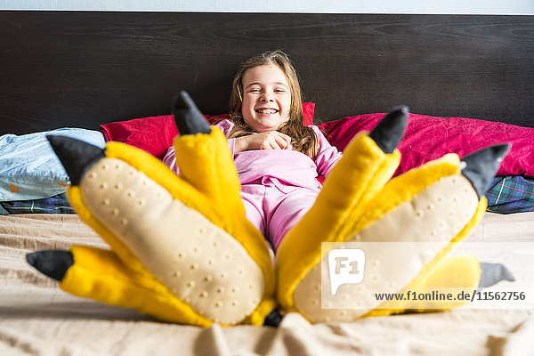 Lächelndes Mädchen liegt auf dem Bett und trägt gelbe Hausschuhe.