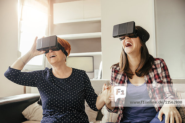 Aufgeregte erwachsene Tochter mit Mutter zu Hause mit VR-Brille
