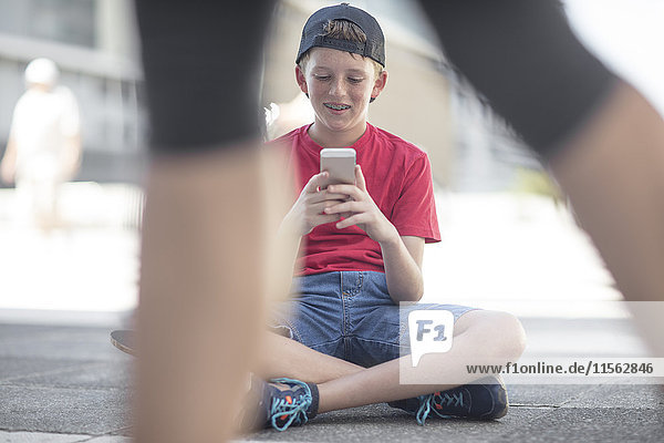 Junge mit Smartphone  sitzend auf Skateboard