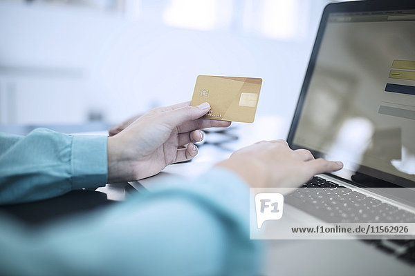 Frau  die eine Kreditkarte hält und am Computer eine Online-Zahlung tätigt.