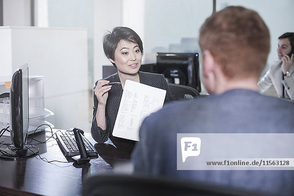 Woman showing sheet of paper to man at desk in office